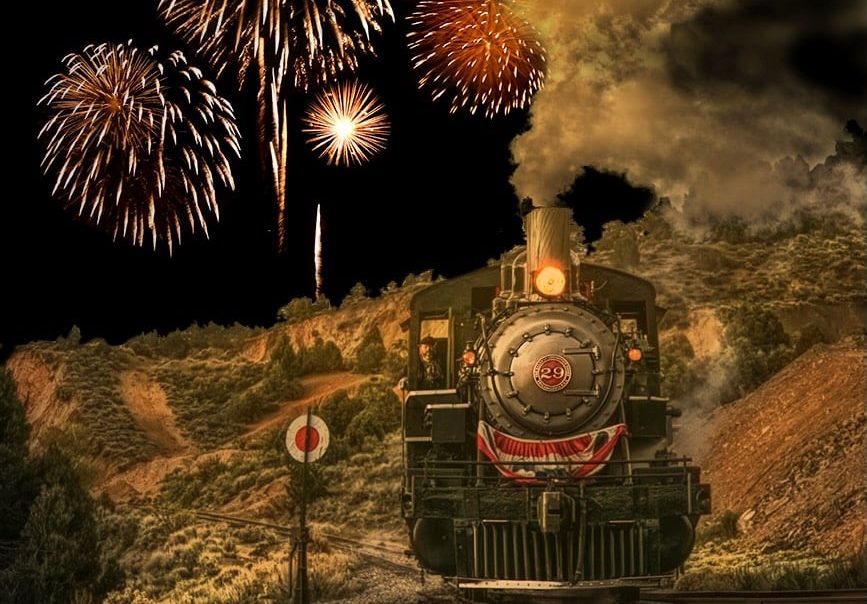 Train-and-SmokeWeb2 | Virginia & Truckee Railroad Steam locomotive on a track at night with fireworks bursting overhead over a rocky landscape.