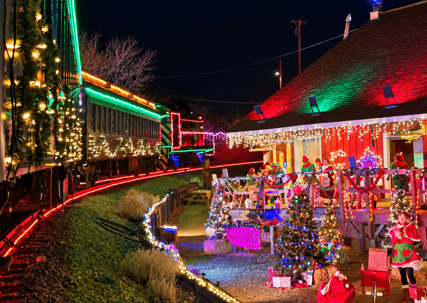 Cristol_image | Virginia & Truckee Railroad | Virginia & Truckee Railroad Night scene of a brightly lit Christmas train display with decorated cars and visitors in festive costumes on a platform.