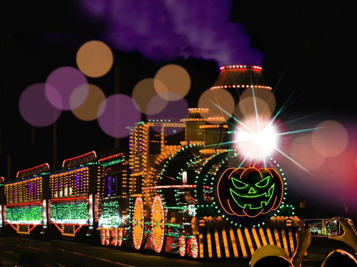 Nighttime Halloween parade float covered in multicolored lights, featuring a glowing neon green jack-o'-lantern at the front and striped base.